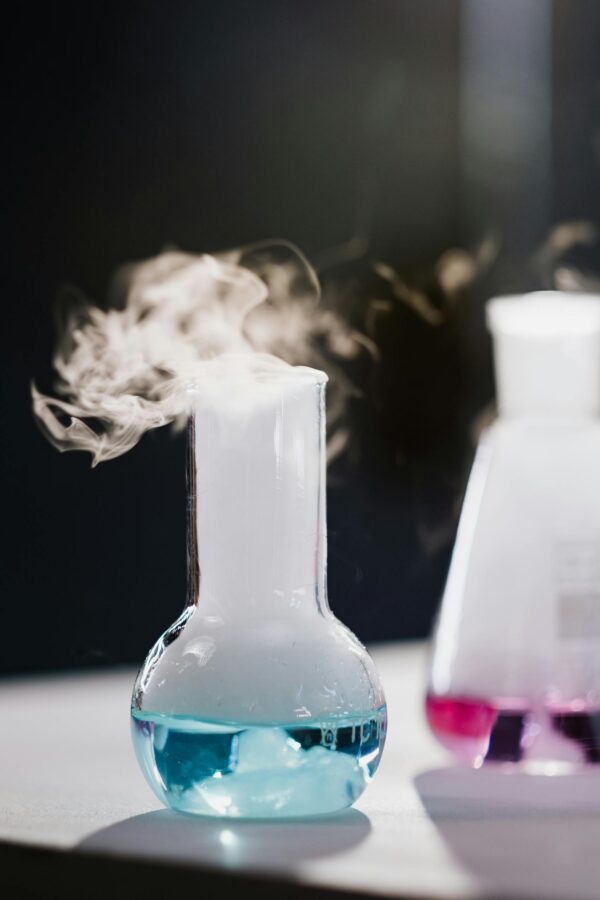 Steam rising from colorful liquid in glass flasks during a lab experiment.